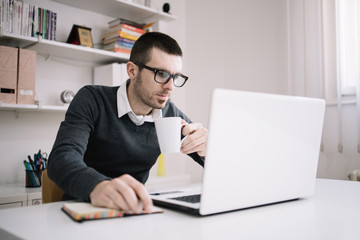 Fototapeta na wymiar Employee holding white mug while using laptop