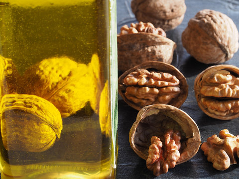 Walnut kernels and a transparent bottle of walnut fruit oil on a dark background, closeup. A bright template of healthy natural products from nuts for proper nutrition.