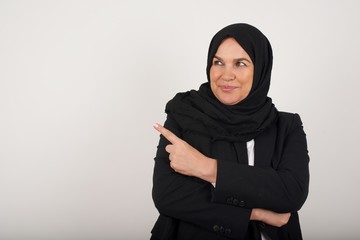 Pretty brunette woman posing on camera with tricky look and gesturing to side. Female designer presenting lovely product with index finger. Gesture concept.