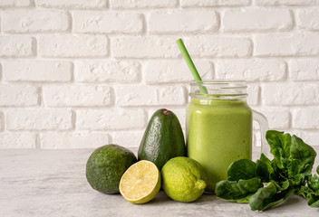Avocado and spinach smoothie in mason jar front view on white brick wall background