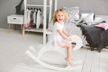  Girl child rides white horse indoor. Child girl happy face enjoy riding horse toy. Kid girl relaxing and having fun riding rocking horse.