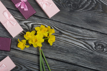A bouquet of yellow daffodils lies on the surface of brushed pine boards. Near cardboard boxes with gifts. Pink and lilac, decorated with ribbon bows.