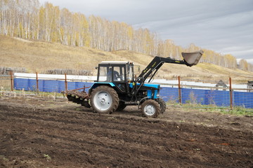 Obraz premium A tractor plows land in a vegetable garden along a fence in the countryside.