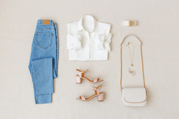 Blue jeans, white shirt, pink heeled sandals,  small cross body bag with chain strap, jewelry, accessories on beige background. Women's stylish spring summer outfit. Trendy clothes. Flat lay, top view