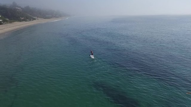 Tilt up aerial, man paddleboards in California