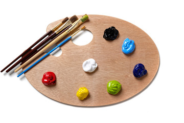 A wooden artists palette with bright colored paint and brushes