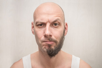 Portrait of a bald man with a half beard. An angry guy thinks to shave him or not. Funny concept of...