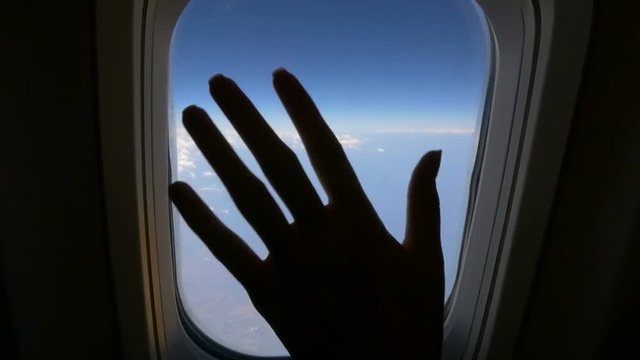 Female hand wave to goodbye from an airplane window