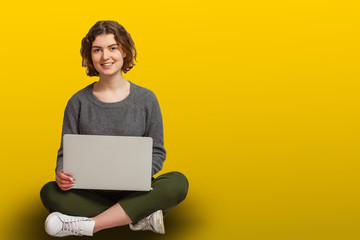 Pretty Indian asian young girl using laptop computer isolated over yellow background