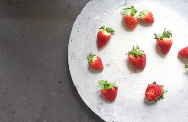 Fresh red strawberries spread out on big light grey rustic plate