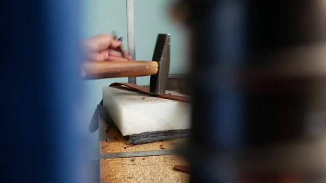 Leather master makes holes in leather for fittings, rivets, install accessories in leather. Using a chisel and a hummer in order to puncture leather. Handmade manufacture