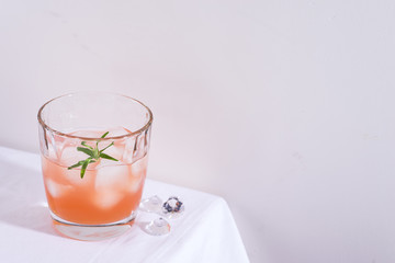 Obraz na płótnie Canvas Pink cocktail with rosemary and ice in glass on a white tablecloth on the table