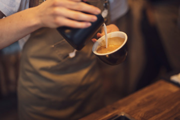 Closeup cup of coffee with pouring milk in a female barista hands