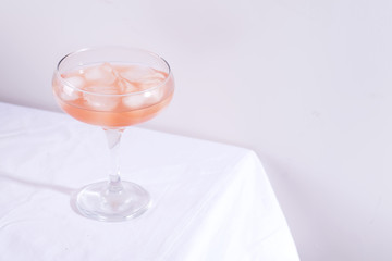 Pink cocktail with rosemary and ice in glass on a white tablecloth on the table