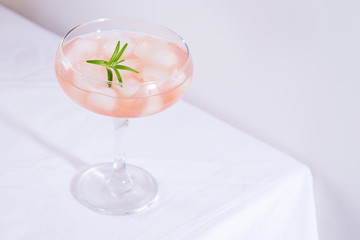 Pink cocktail with rosemary and ice in glass on a white tablecloth on the table