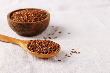 Flax seeds in a wooden spoon and bowl on a natural linen tablecloth
