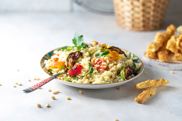 Tasty vegetarian couscous with tomatoes, zucchini, yellow and red peppers, cashew nuts and herbs on a light background. Vegan food. Arabic traditional food. The concept of organic food.
