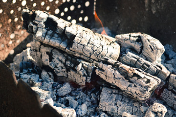 Fototapeta na wymiar Smoldering ashes of a bonfire. Incandescent orange and red embers texture. Dark background. Fire flame and Firewood in a brick barbecue. A place for cooking meal outside. smouldering embers on a surfa