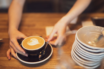 Your cup of latte is ready, barista hands put it on the table