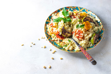 Tasty vegetarian couscous with tomatoes, zucchini, yellow and red peppers, cashew nuts and herbs on a light background. Vegan food. Arabic traditional food. The concept of organic food.