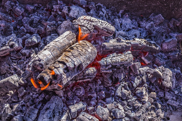 Smoldering ashes of a bonfire. Incandescent orange and red embers texture. Dark background. Fire flame and Firewood in a brick barbecue. A place for cooking meal outside. smouldering embers on a surfa