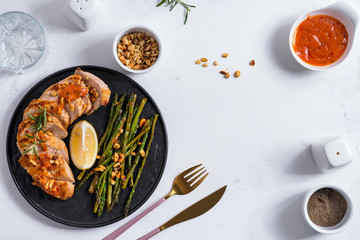 grilled chicken breast fillet with asparagus, sauce and lemon in slate plate and white stone...