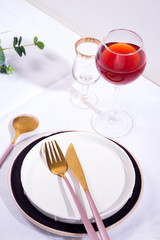 Tableware and decorations for serving a festive table. Plates, red wine glass and cutlery on white textile background.