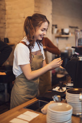 Young and cheerful barista woman make a coffee in the cafeteria
