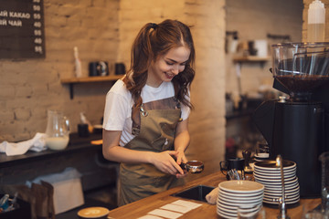 Young and cheerful barista woman make a coffee in the cafeteria