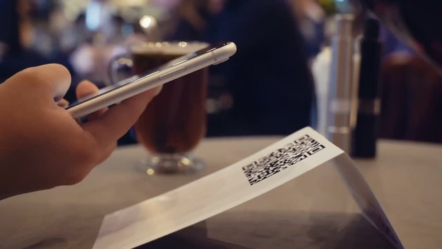 Scanning QR code with smart phone. The man reads the bar code using the application on the smartphone in restaurant