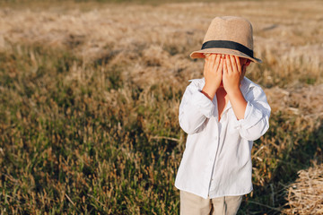 blond little boy in straw hat playing in field on mowed hay. summer, sunny weather, farming. happy childhood.