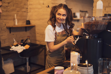 Young and cheerful barista woman make a coffee in the cafeteria