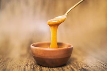 Manuka honey spoon dipped in golden liquid natural superfood on wooden background.