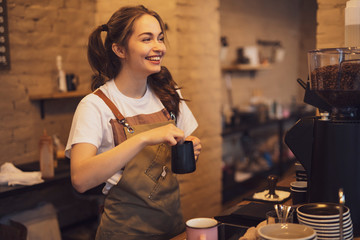 Young and cheerful barista woman make a coffee in the cafeteria