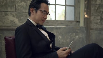 Asian groom sitting on a red chair using smartphone are smiling and happy in studio. Handheld shot. Real life - Powered by Adobe