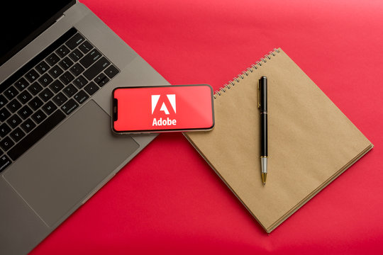 Tula, Russia - February 07, 2020: Logo Adobe on a smartphone near modern laptop on red background