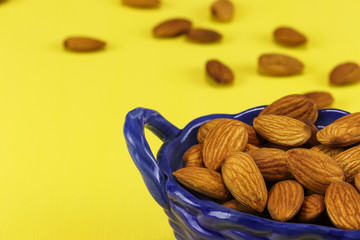 Almond nuts lie in a blue glass basket and on a yellow surface