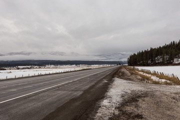 Fototapeta na wymiar Empty highway in cold of winter with fog shrouded mountains and trees on overcast day