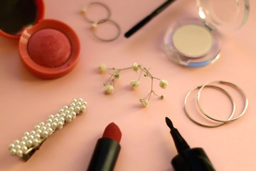 Fototapeta na wymiar Beauty products and fashionable accessories on pale pink background: blush, mascara, eyeliner, lipstick,k rings, hoop earrings, beret and gypsophila flowers. Selective focus.