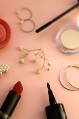 Beauty products and fashionable accessories on pale pink background: blush, mascara, eyeliner, lipstick,k rings, hoop earrings, beret and gypsophila flowers. Selective focus.