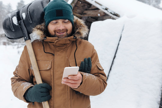 Portrait of smiling man with snow shovel looking at cell phone