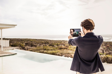 Young man in business jacket taking a selfie in a beach house with a pool