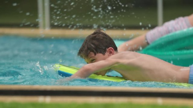 Young boy swimming at the pool on top of surfer board
