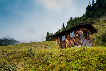 A small wooden house or hut in the Alps mountains in the south of Germany with a blue sky and a beautiful green field.