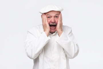 Joyful senior chef cook or baker man in chefs hat posing excited. It is so delicious receipt. Studio shot