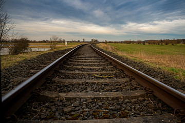 Obraz premium Eisenbahnschienen durch ein Wiesengelände in der Abenddämmerung