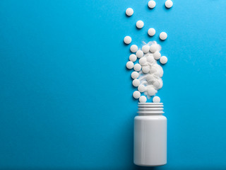 White pills spilled from a white bottle on a blue background