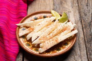 Mexican jicama  cutted with chili powder on wooden background