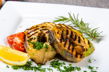 Sturgeon steak on the grill. A few pieces of grilled sturgeon steak lie on a square plate....