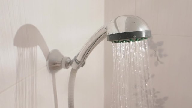 Water streams. Metal shower head in white bathroom. Working plumbing equipment.
